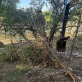 Excavator clears flood debris along a Kerrville riverbank