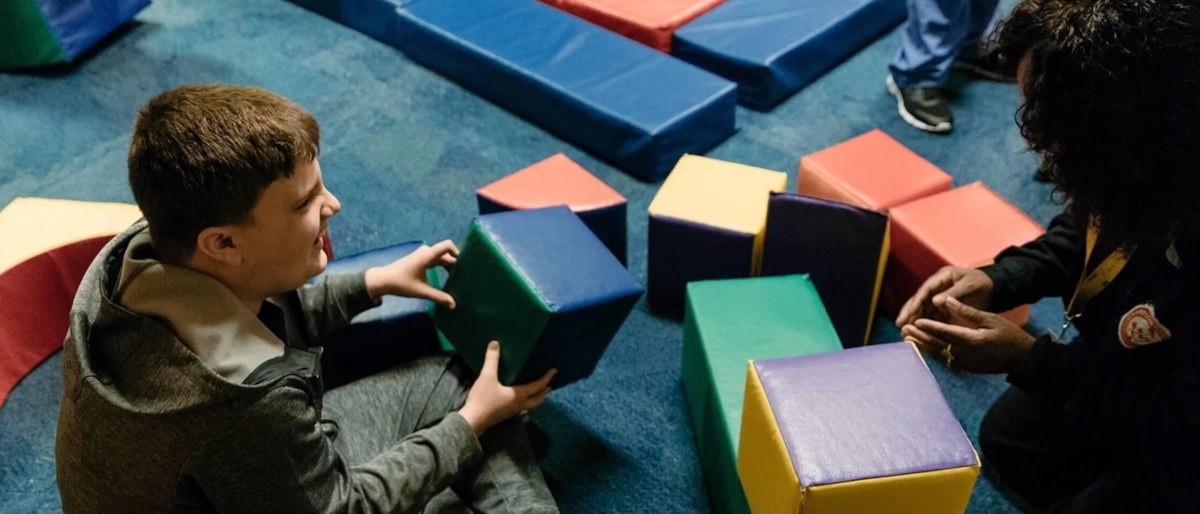 Volunteer engages a child with soft blocks at Champions Club