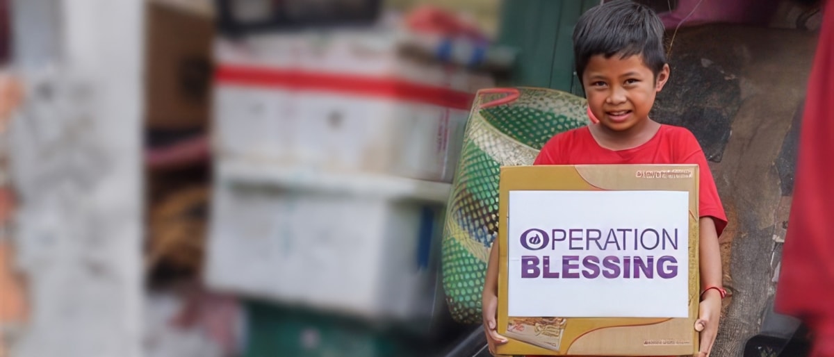 Child holds an Operation Blessing relief box in the community